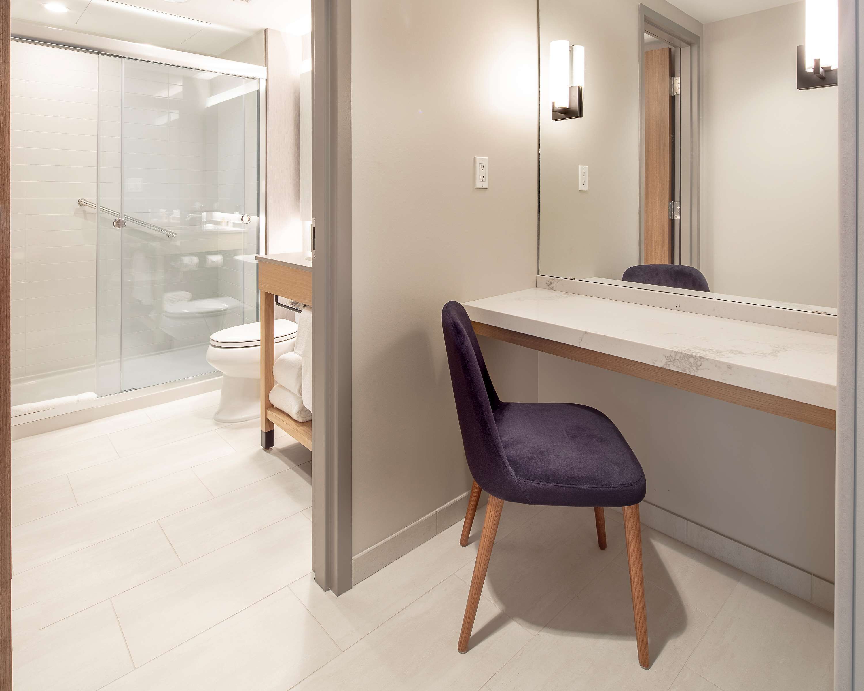 Un baño moderno con cabina de ducha de vidrio, inodoro blanco y tocador con espejo.