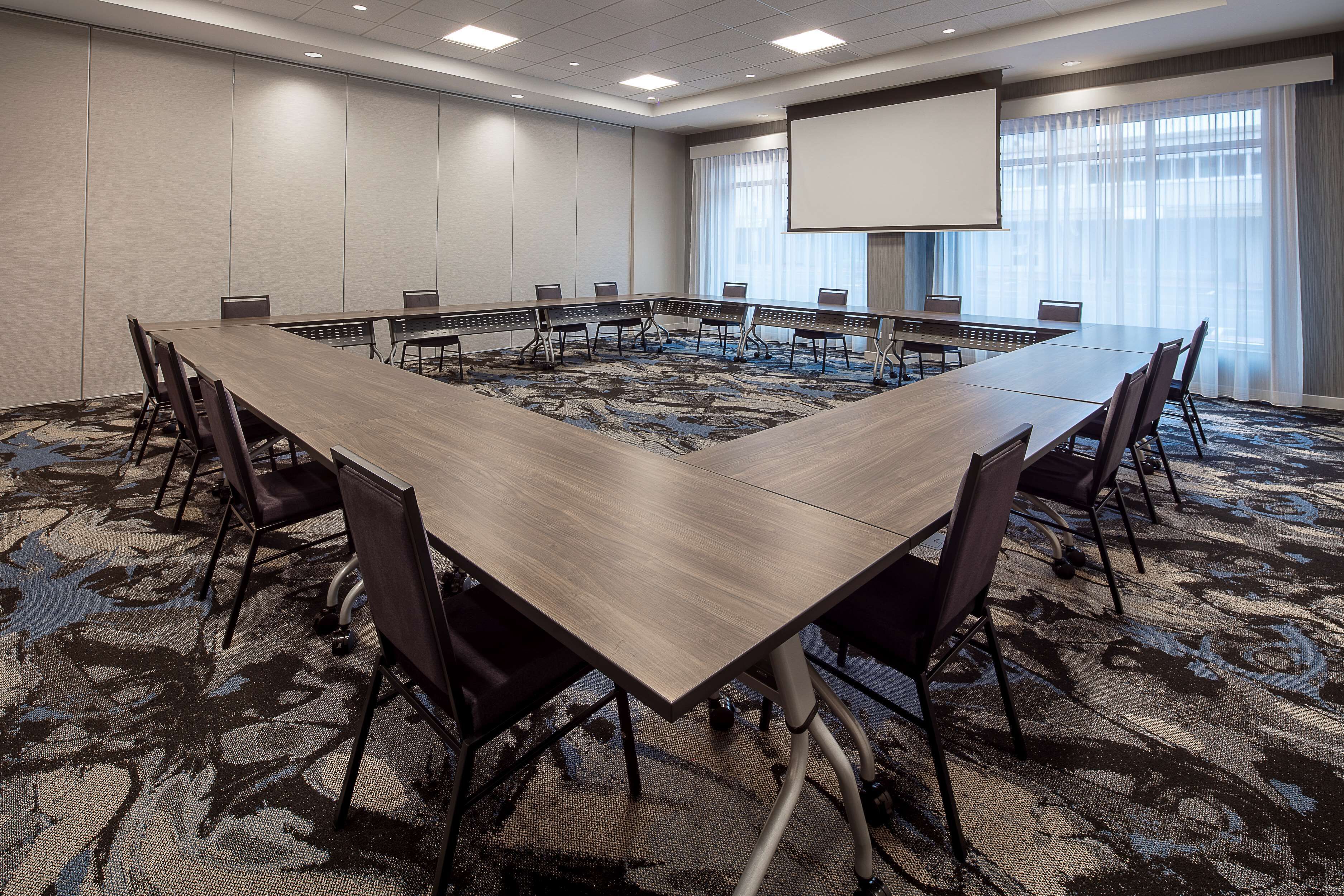A conference room with a large table, chairs, a projector screen, and a carpeted floor.