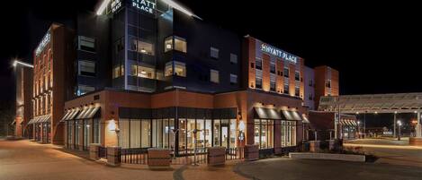 Un hotel de varios pisos con un diseño moderno, que presenta un llamativo letrero de 'Hyatt Place', un área exterior cubierta y un frente de ladrillo.