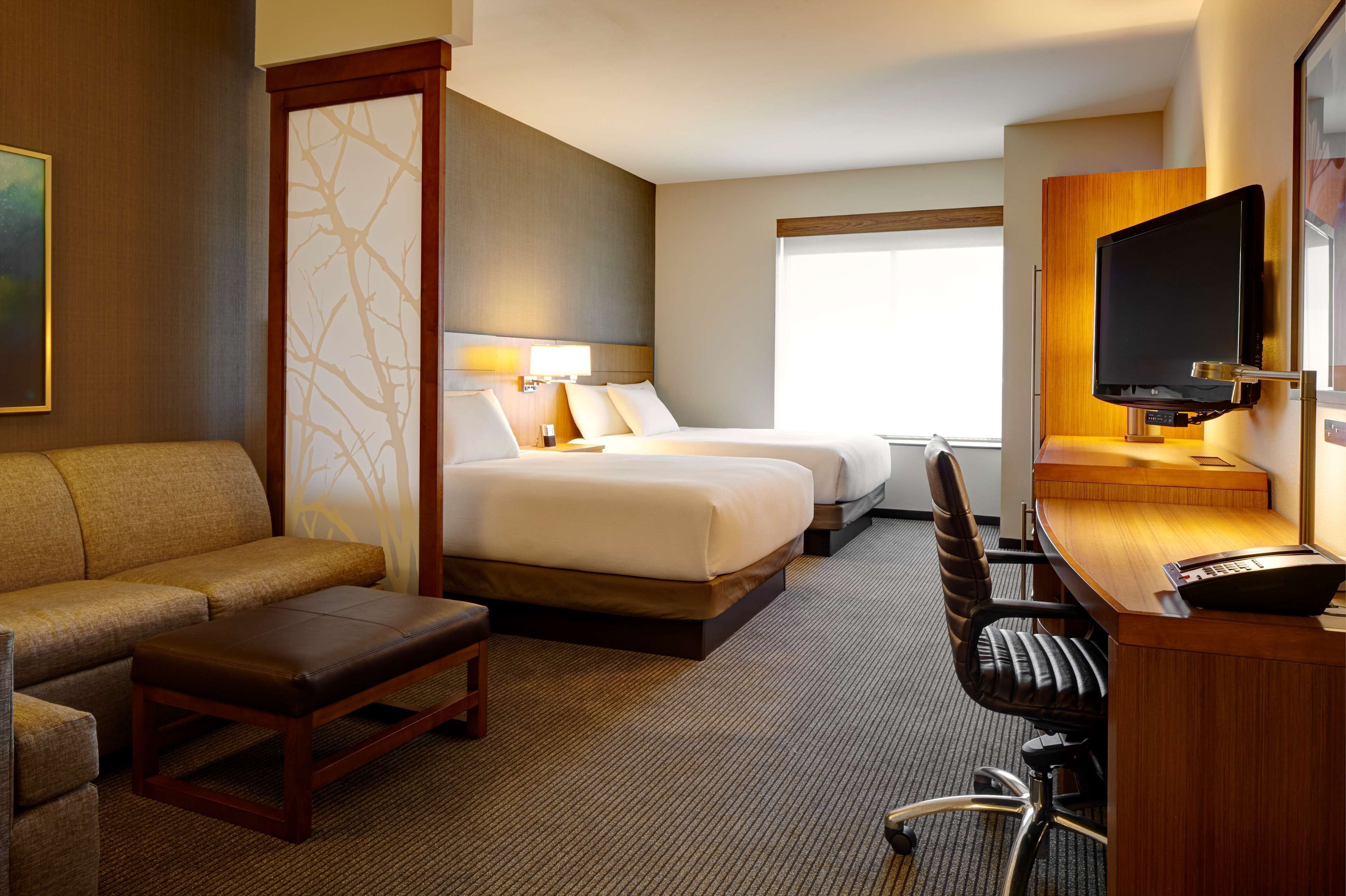 A hotel room with two beds, a sofa, a desk with a computer, and a TV.
