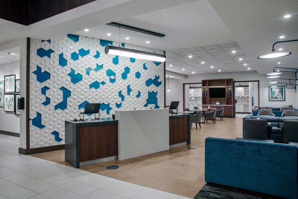A modern reception area with a geometric patterned wall, a reception desk, and a seating area with blue upholstered sofas. - Hyatt Place Titusville / Kennedy Space Center (Titusville)