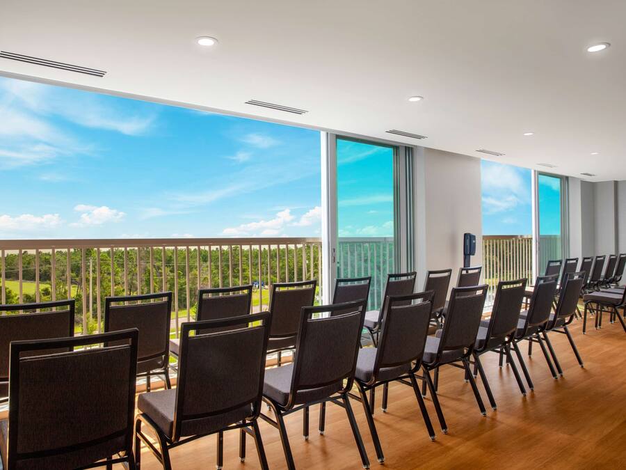 A conference room with a long table and chairs, large windows with a view of greenery, and a modern ceiling design.