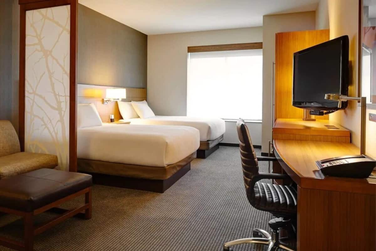 A hotel room with two beds, a sofa, a desk with a computer, and a TV.