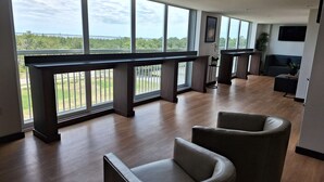 Um quarto espaçoso com grandes janelas, piso de madeira e móveis modernos, incluindo um sofá e poltronas.