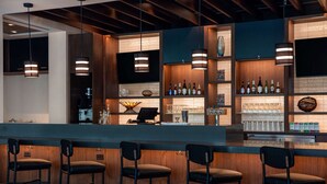 Uma área de bar moderna com detalhes em madeira, banquetas e diversos frascos e copos em prateleiras.