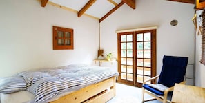 A room with a wooden bed, a chair, a window with a view, and a door. - Alpages Madarao (Myoko)