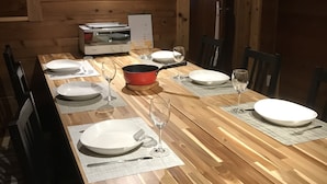 A wooden dining table set with plates, glasses, and a red pot. - Alpages Madarao (Myoko)