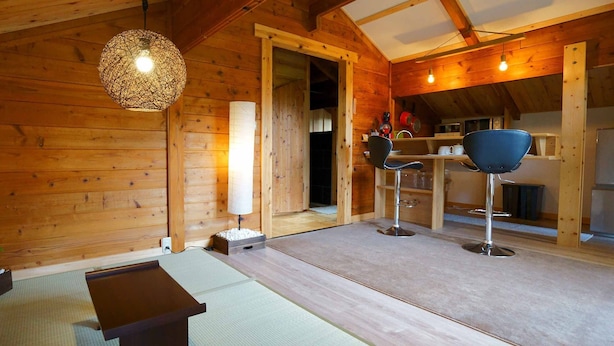 A wooden interior with a tatami mat floor, a traditional Japanese table, a hanging light fixture, and a kitchen area with a microwave and a sink. - Alpages Madarao (Myoko)