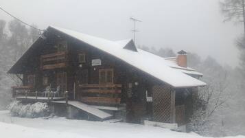 A wooden cabin with a steeply pitched roof, surrounded by snow-covered ground and trees.