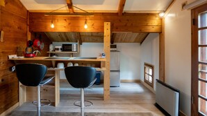 A compact kitchen with wooden walls, a dining area with two black chairs, and a window providing natural light. - Alpages Madarao (Myoko)