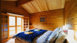A wooden cabin room with a bed, a small window, and a door leading to a balcony. - Alpages Madarao (Myoko)