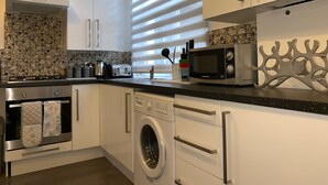 A modern kitchen with white cabinets, a stainless steel range, a washing machine, and a microwave. - Roath Retreat (Cardiff)