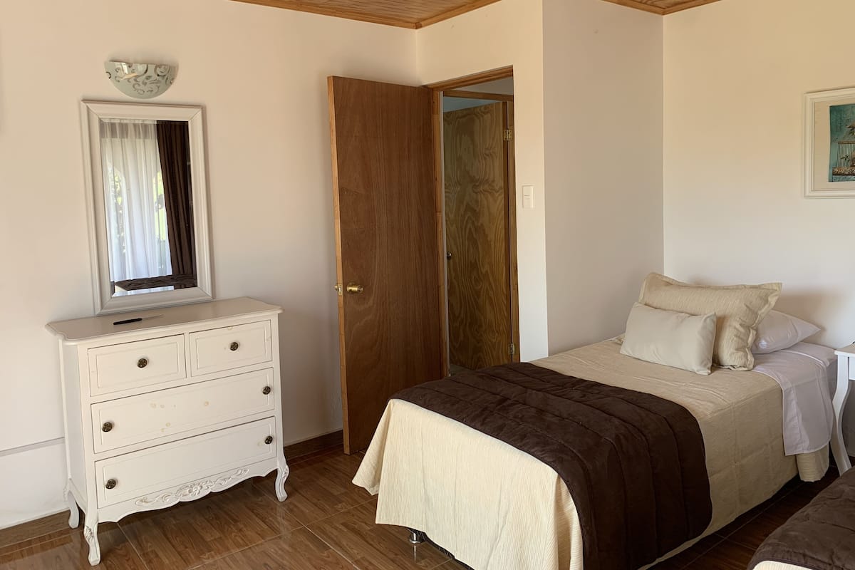 Een slaapkamer met een bed, een dressoir, een deur en een raam met gordijnen.