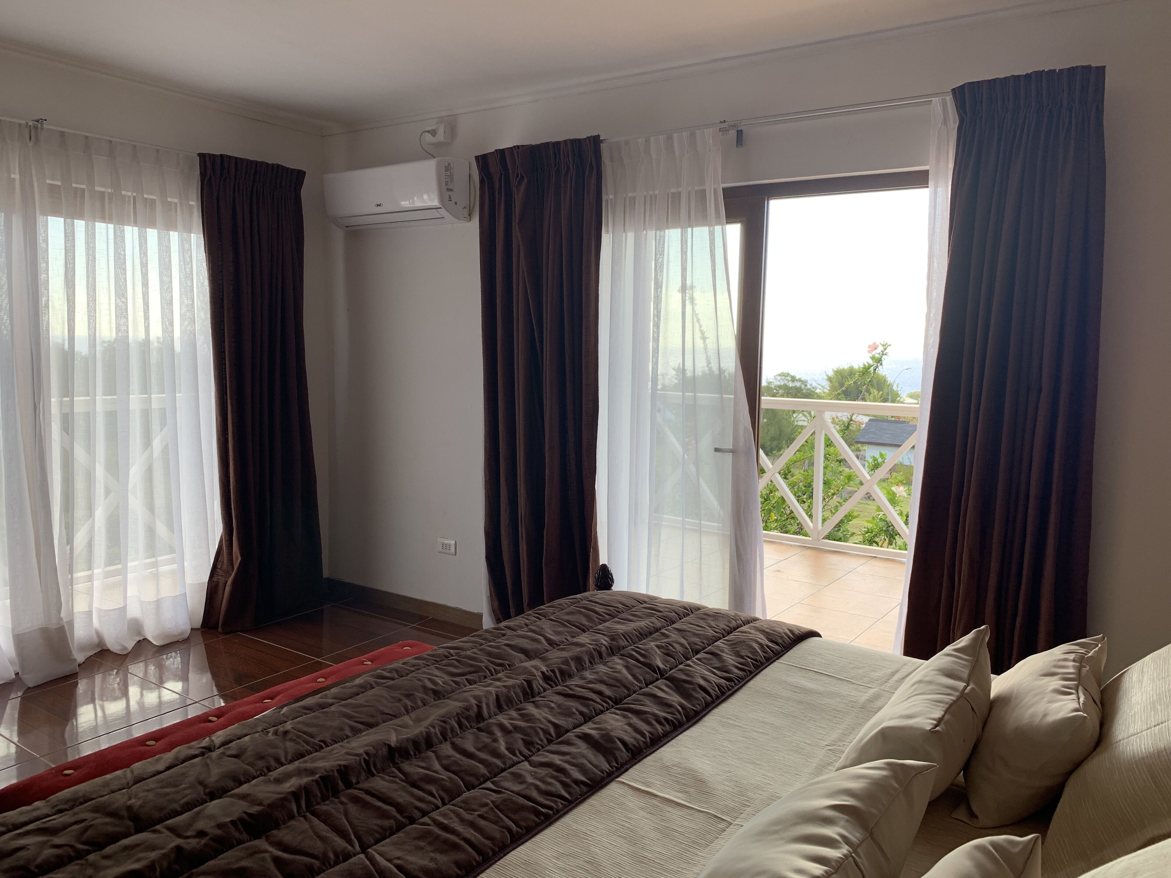 A hotel room with a bed, a balcony with a railing, and an air conditioning unit on the wall.