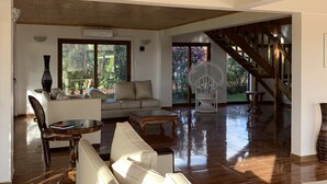 A spacious living room with a wooden ceiling, a sofa, a coffee table, and a chair. There is a staircase leading to an upper level. - Hotel Teanehi (Hanga Roa)