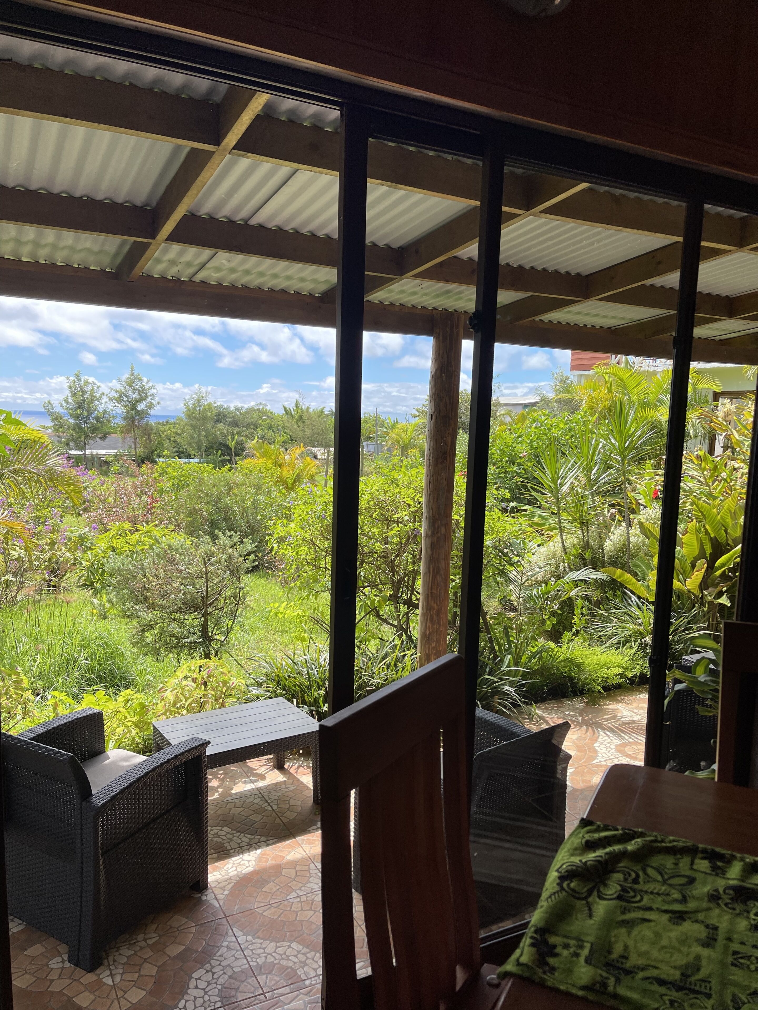 A covered outdoor area with wicker furniture and a view of lush greenery and a body of water.