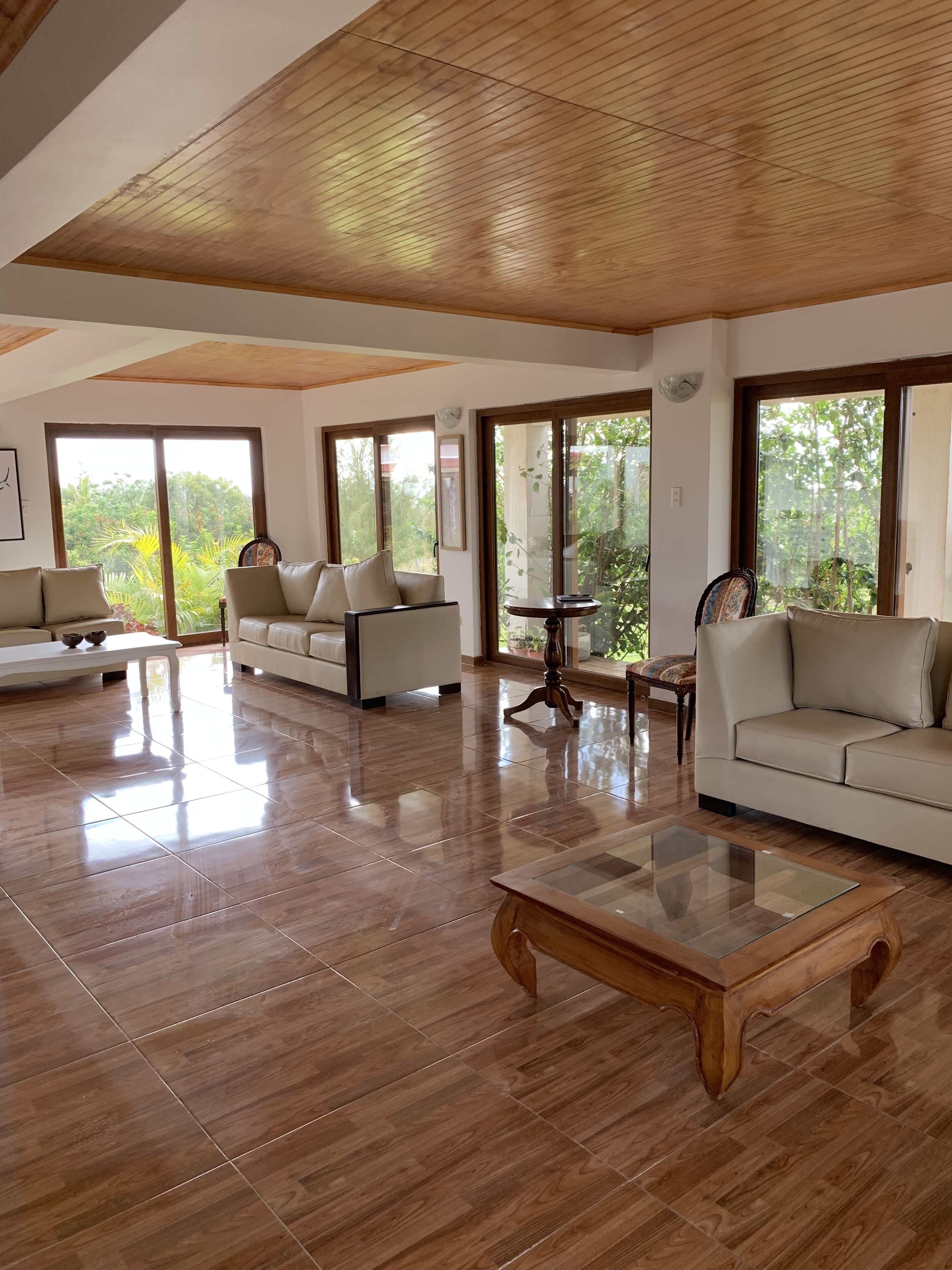 A spacious living room with a high ceiling, large windows, and a polished wooden floor.