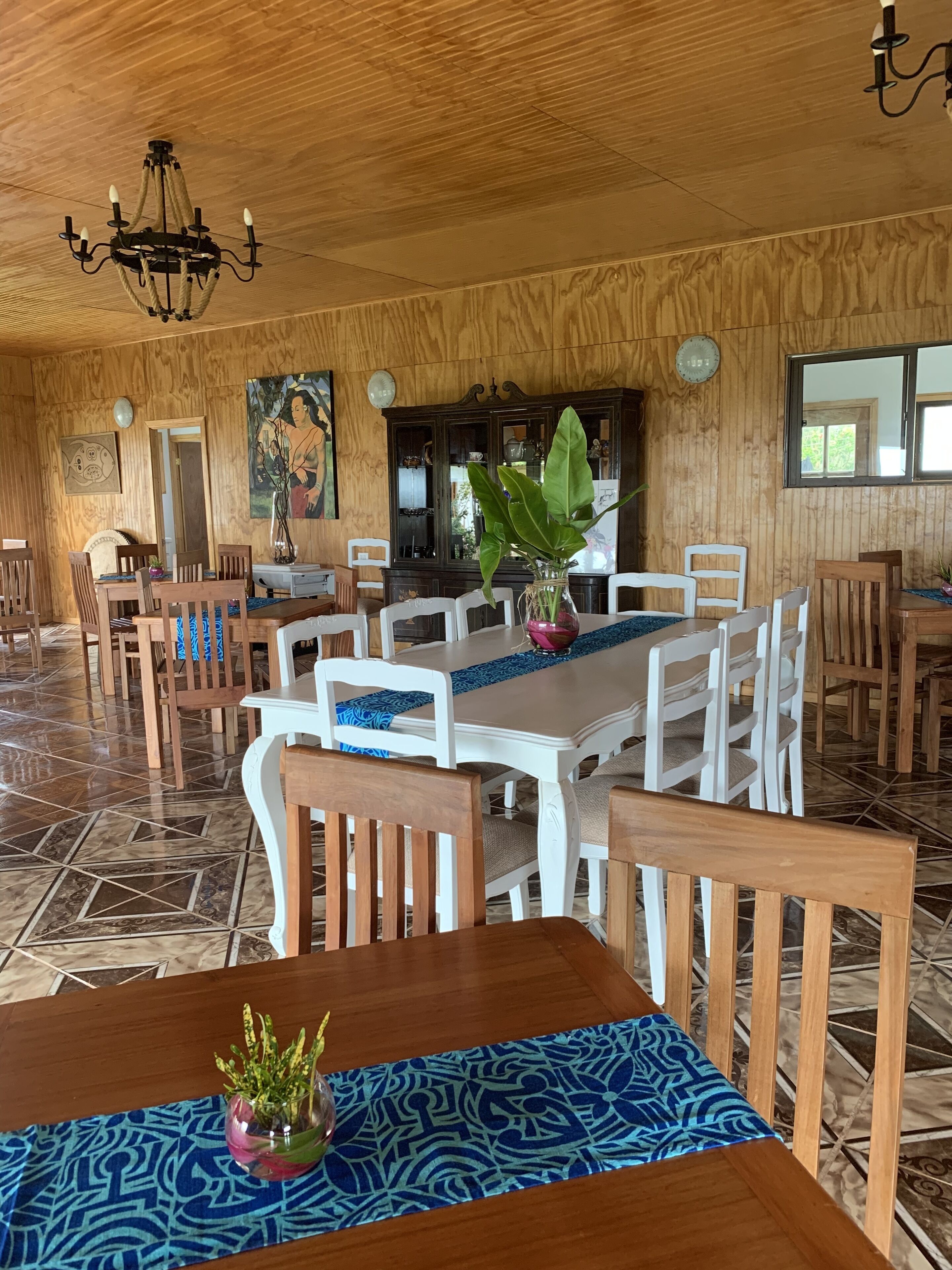 Ein Essbereich mit einem Holztisch, Stühlen, einer Chandelüster und einer großen Pflanze.