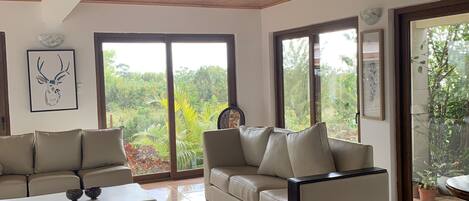 Amplia sala de estar con techo de madera, ventanas grandes, un sofá color beige y una mesa de centro blanca.