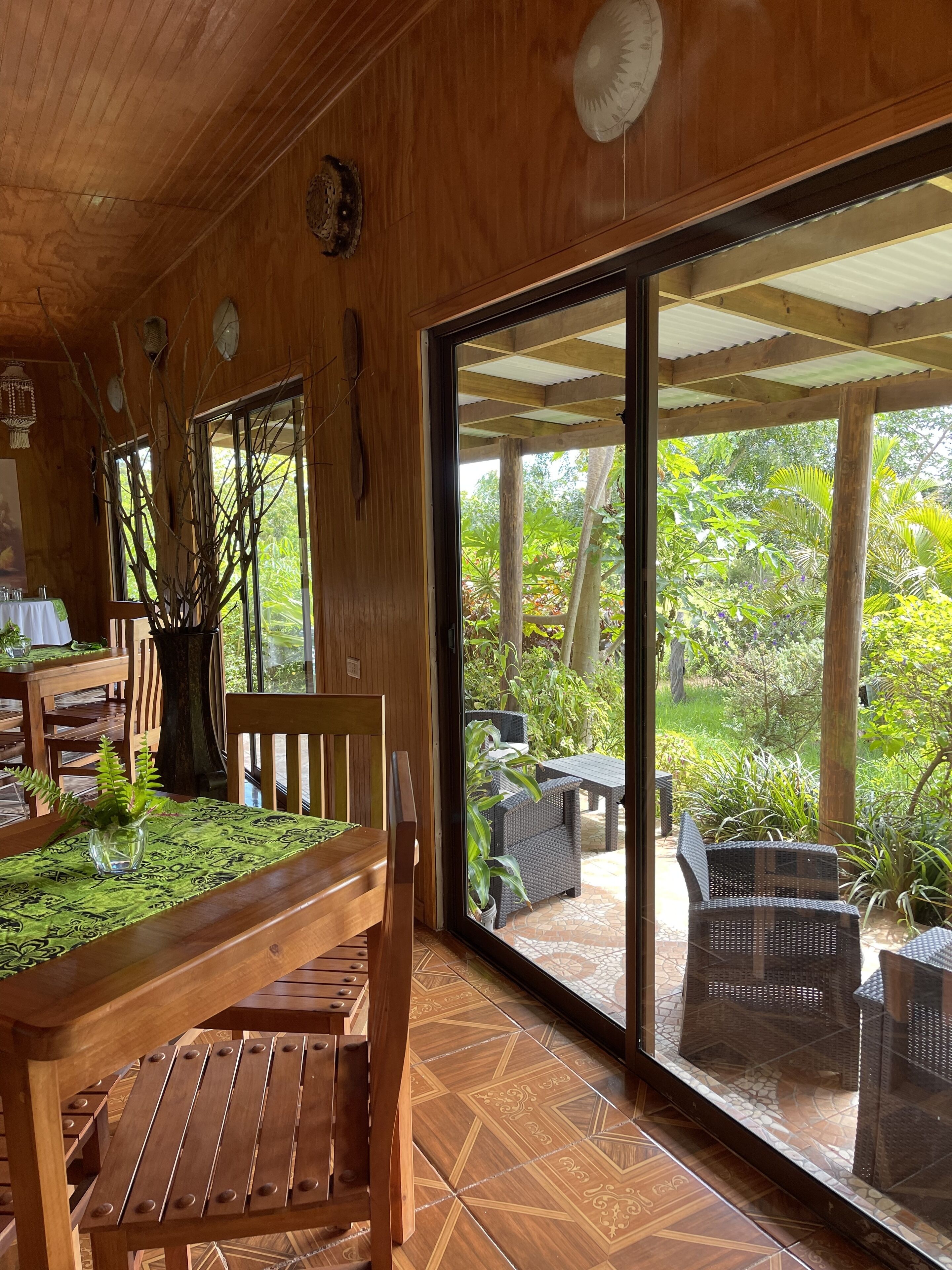 A wooden interior with a dining area featuring a table and chairs, a large window with a view of the garden outside.