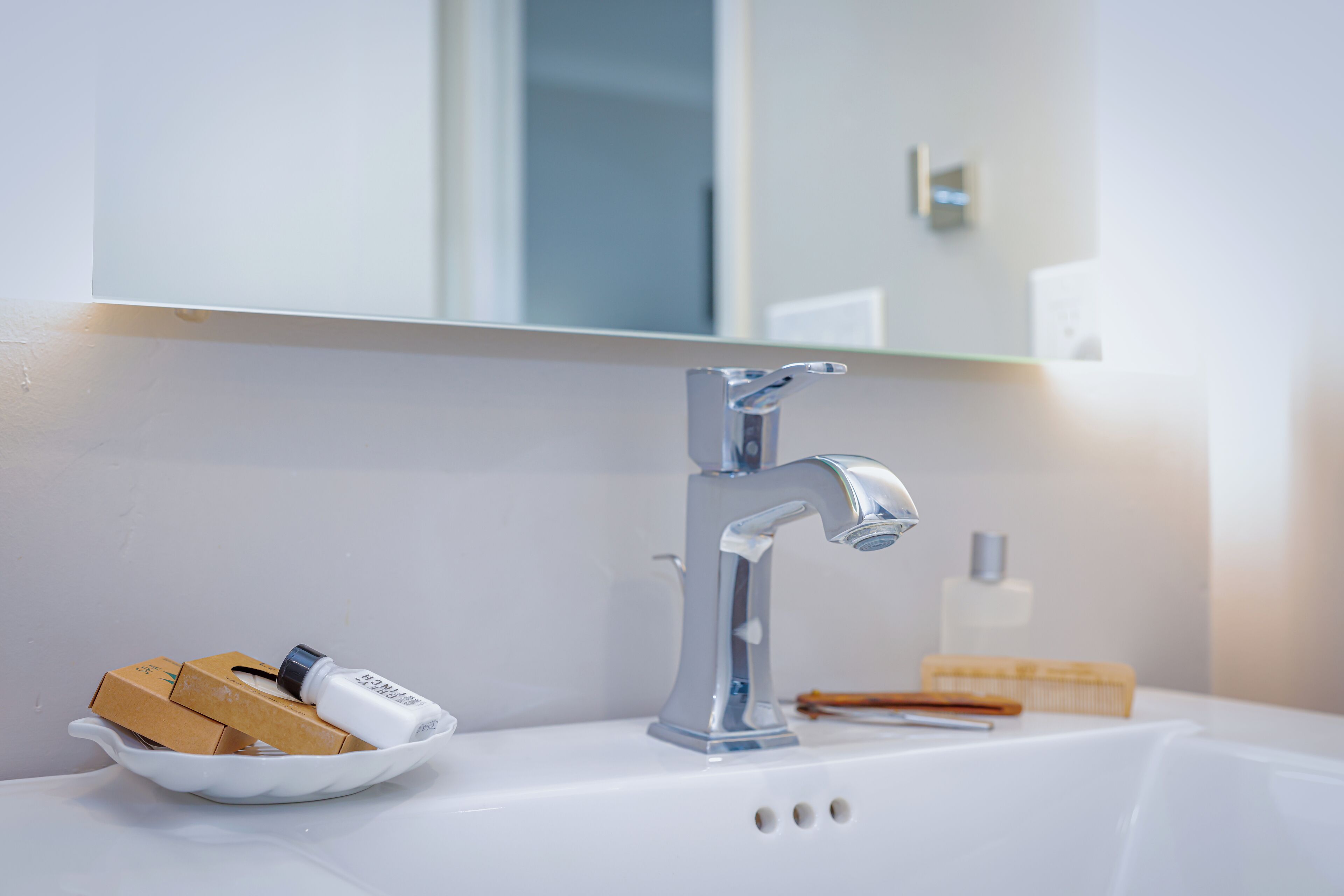 A bathroom sink with a chrome faucet, a bowl containing toiletries, and a mirror above the sink.