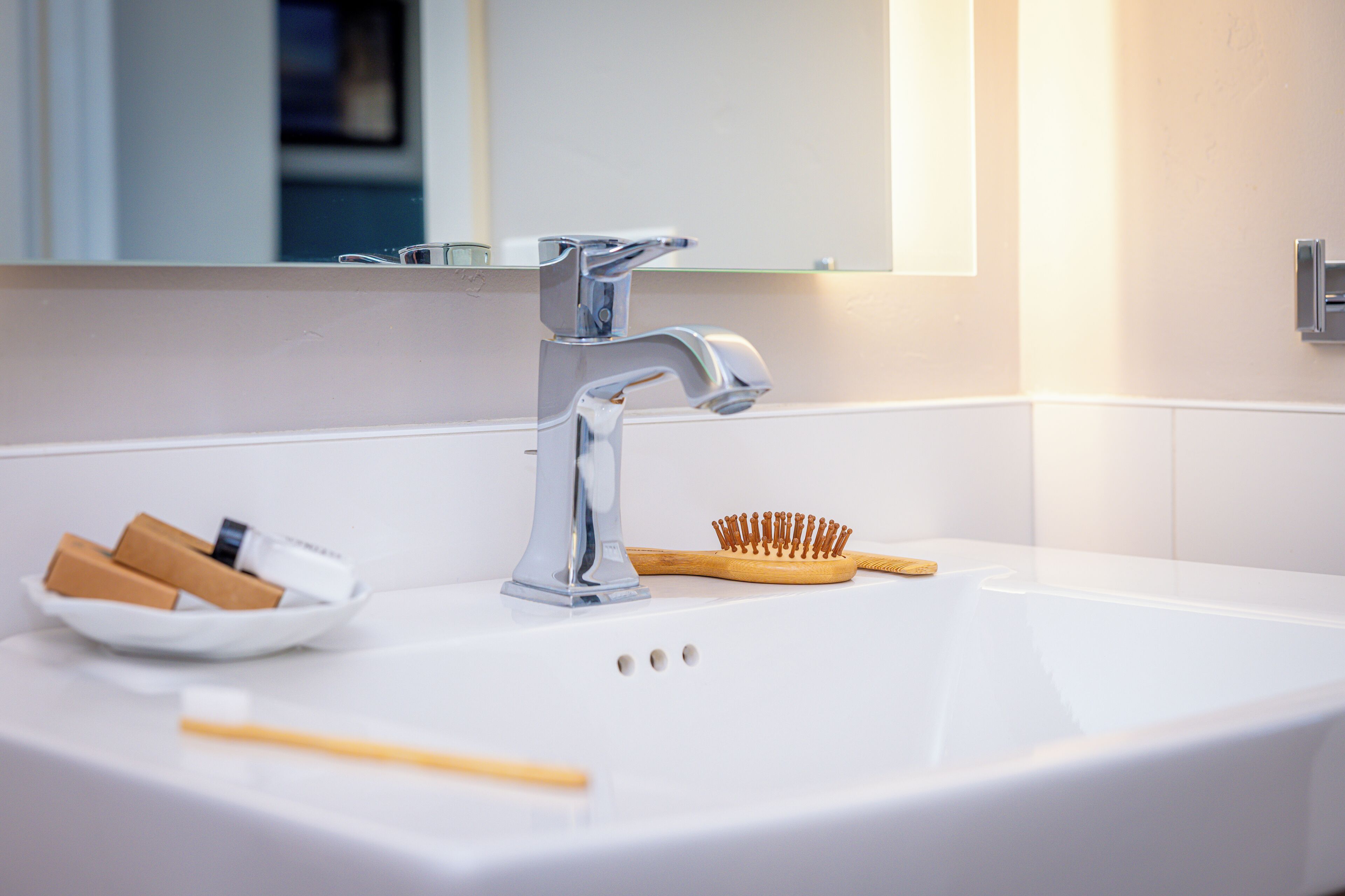 A bathroom sink with a chrome faucet, a bowl of toiletries, and a wooden brush.