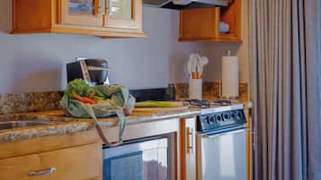 A kitchen with wooden cabinets, a stove, an oven, a sink, and a countertop with a bag of vegetables.