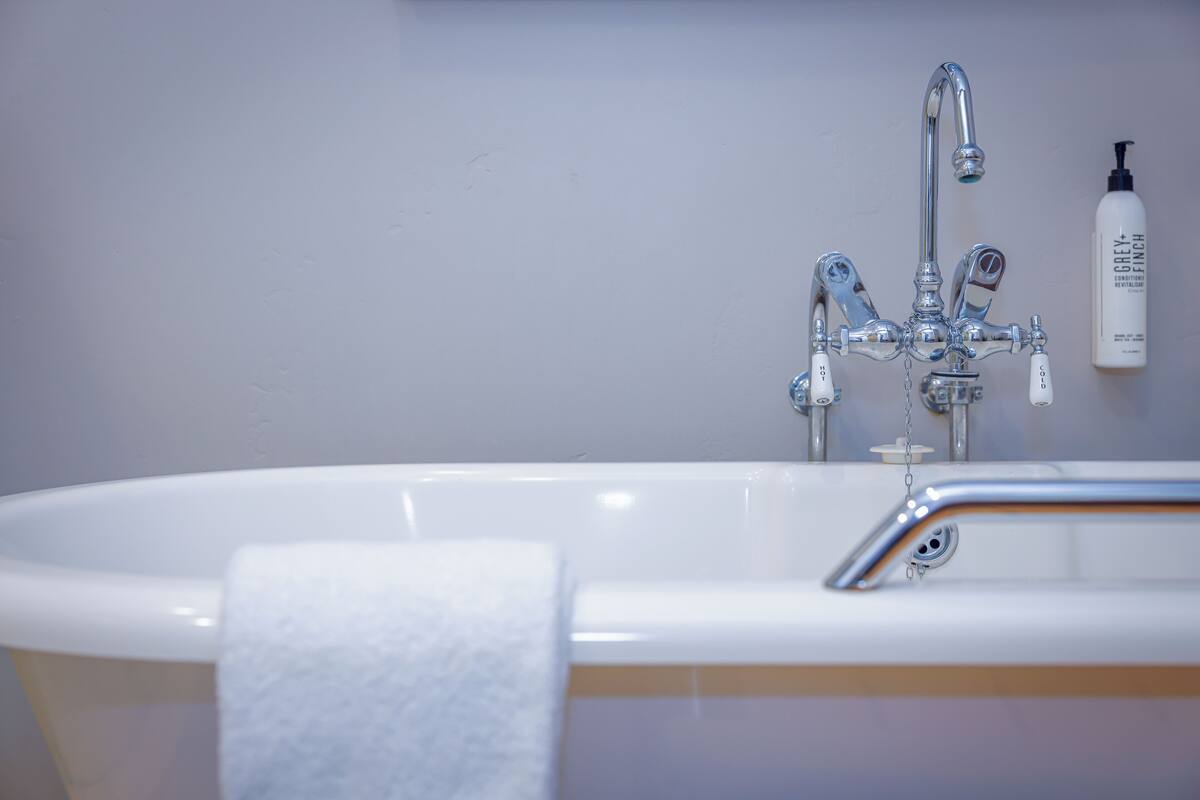 A bathroom with a white bathtub, a chrome faucet, and a bottle of Grey Finch conditioner on the wall.
