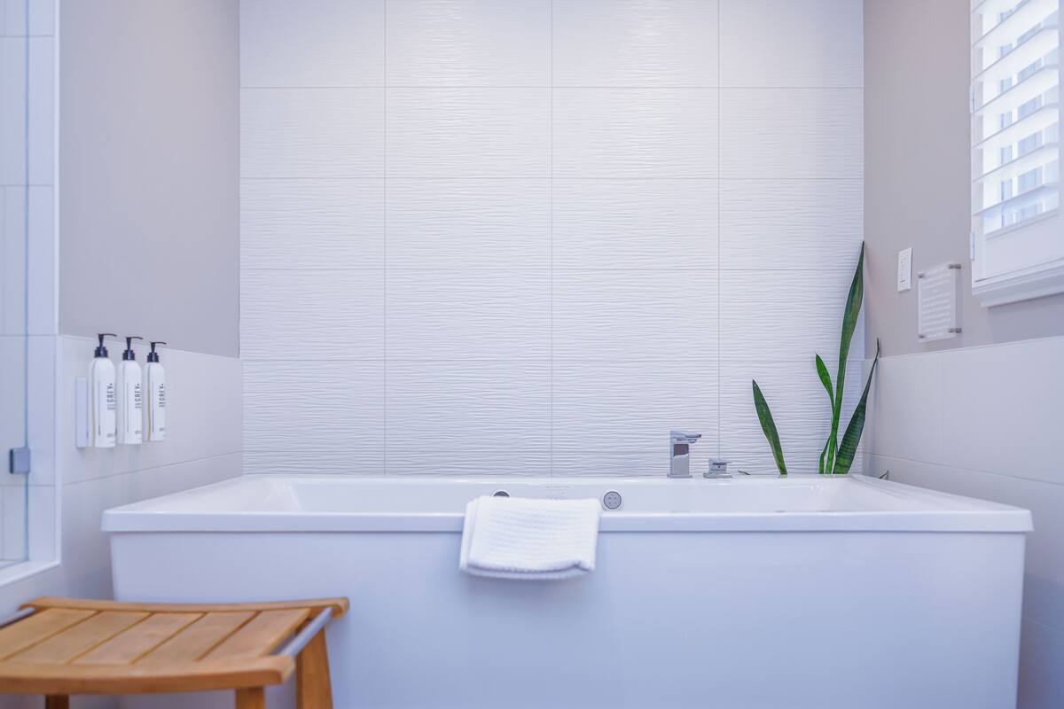 A modern bathroom with a white bathtub, a wooden bench, and a potted plant.