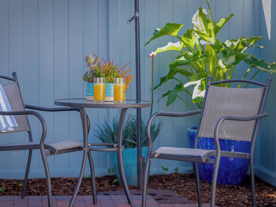 Two metal chairs with blue and white striped towels, a small round table with two glasses of orange juice, and a potted plant in the background.