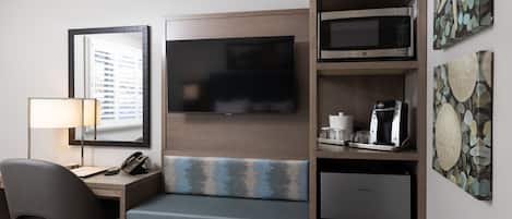 A hotel room with a bed, a desk with a lamp, a telephone, a television, a microwave, a coffee maker, and a small refrigerator.