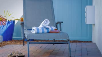 A chair with a rolled towel and a bag, and a pair of shoes on a brick pathway.