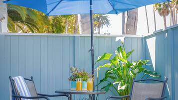 Un patio con dos sillas de metal, una mesa, una sombrilla azul y una planta en maceta.