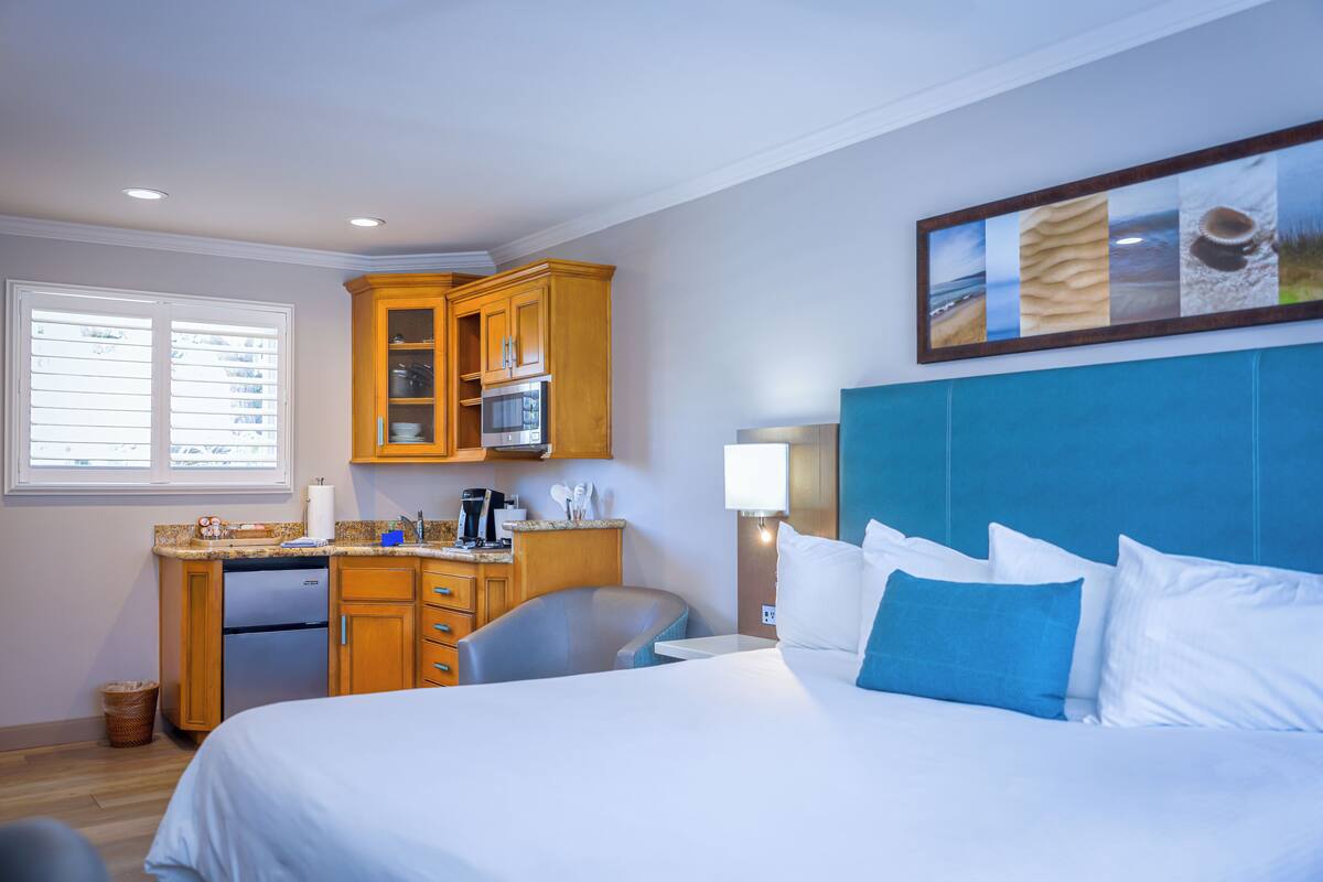 A hotel room with a bed, a desk with a refrigerator, a microwave, and a lamp.