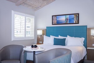 Quarto de hotel com uma cama grande, duas mesas de cabeceira, uma mesa redonda e uma cadeira.