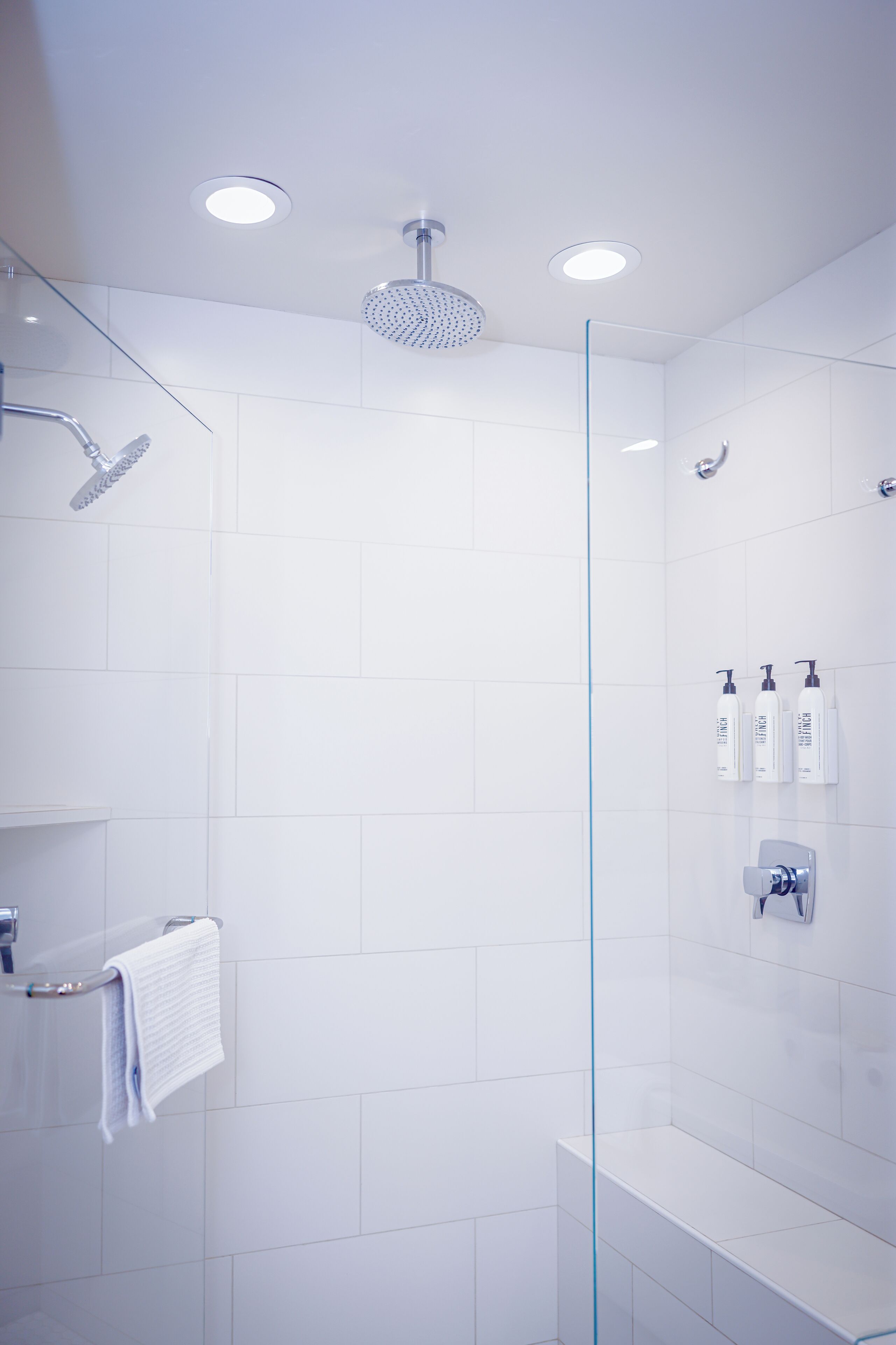A modern shower with a glass partition, a towel rack, and a shelf with toiletries.