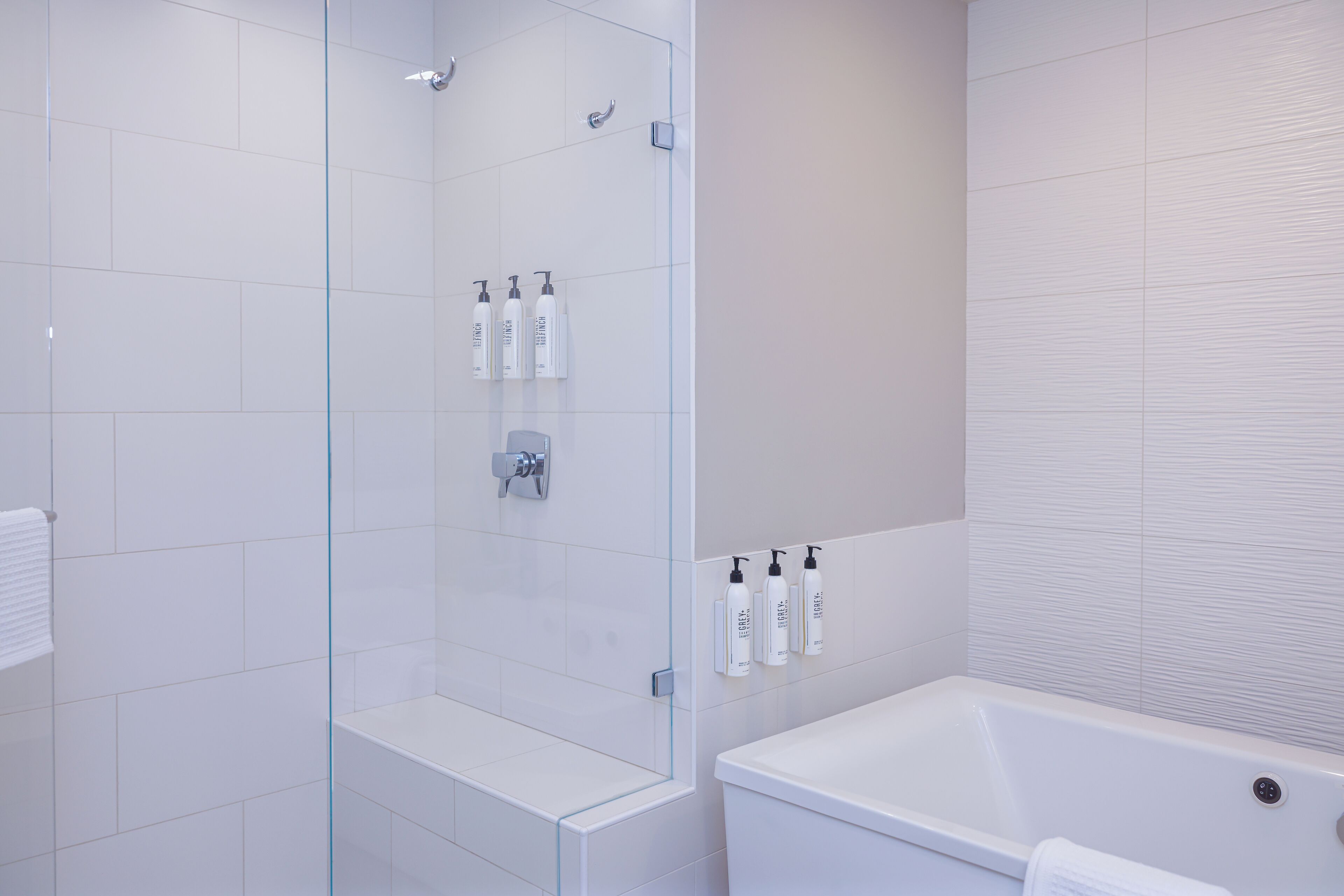 Une salle de bain moderne avec une douche à parois de verre, une baignoire blanche et des articles de toilette rangés avec soin sur un meuble mural.