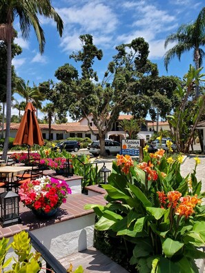 Un espace extérieur ensoleillé, aménagé avec des tables et des chaises, et entouré d’une végétation tropicale luxuriante et de fleurs.
