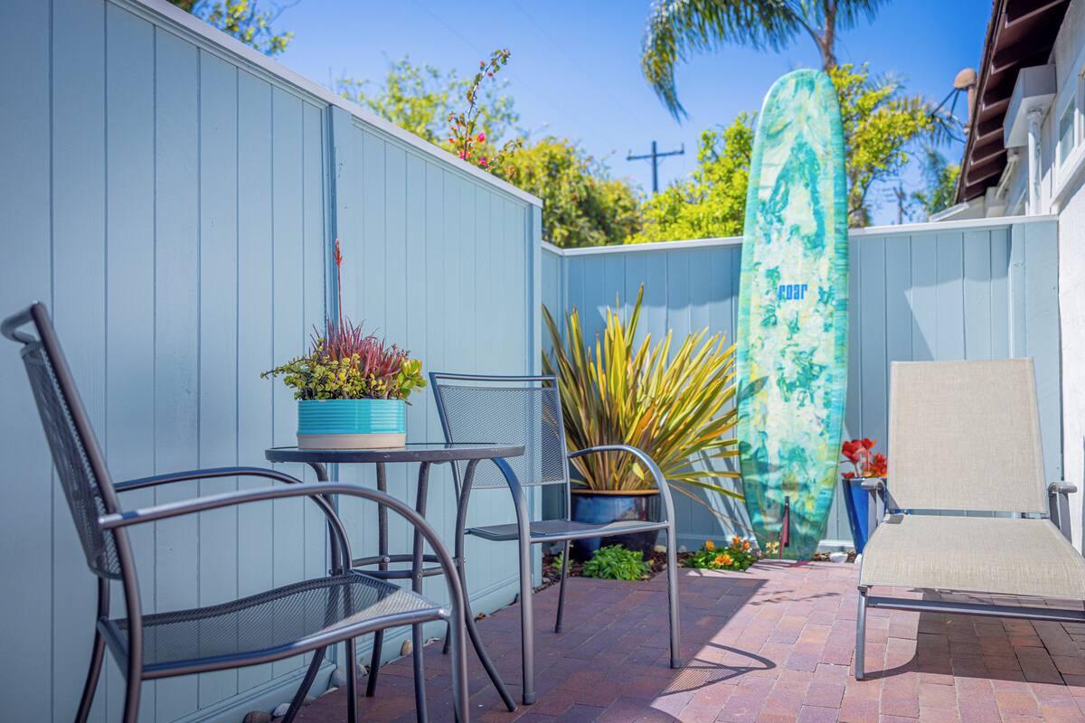 A patio with metal chairs, a table, and a surfboard leaning against a wall.