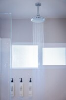 A shower with a rain head, a window, and three bottles of Grey Finch shampoo.