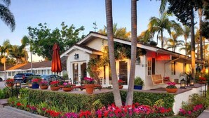A hotel with a patio area, outdoor seating, and a well-maintained garden with flowers and palm trees. - Marina Beach Hotel (Santa Barbara)