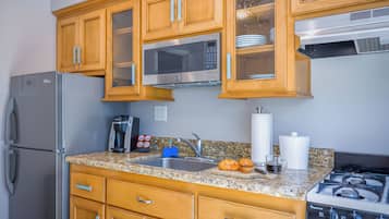 A kitchen with wooden cabinets, a stainless steel refrigerator, a microwave, a stove, and a granite countertop.