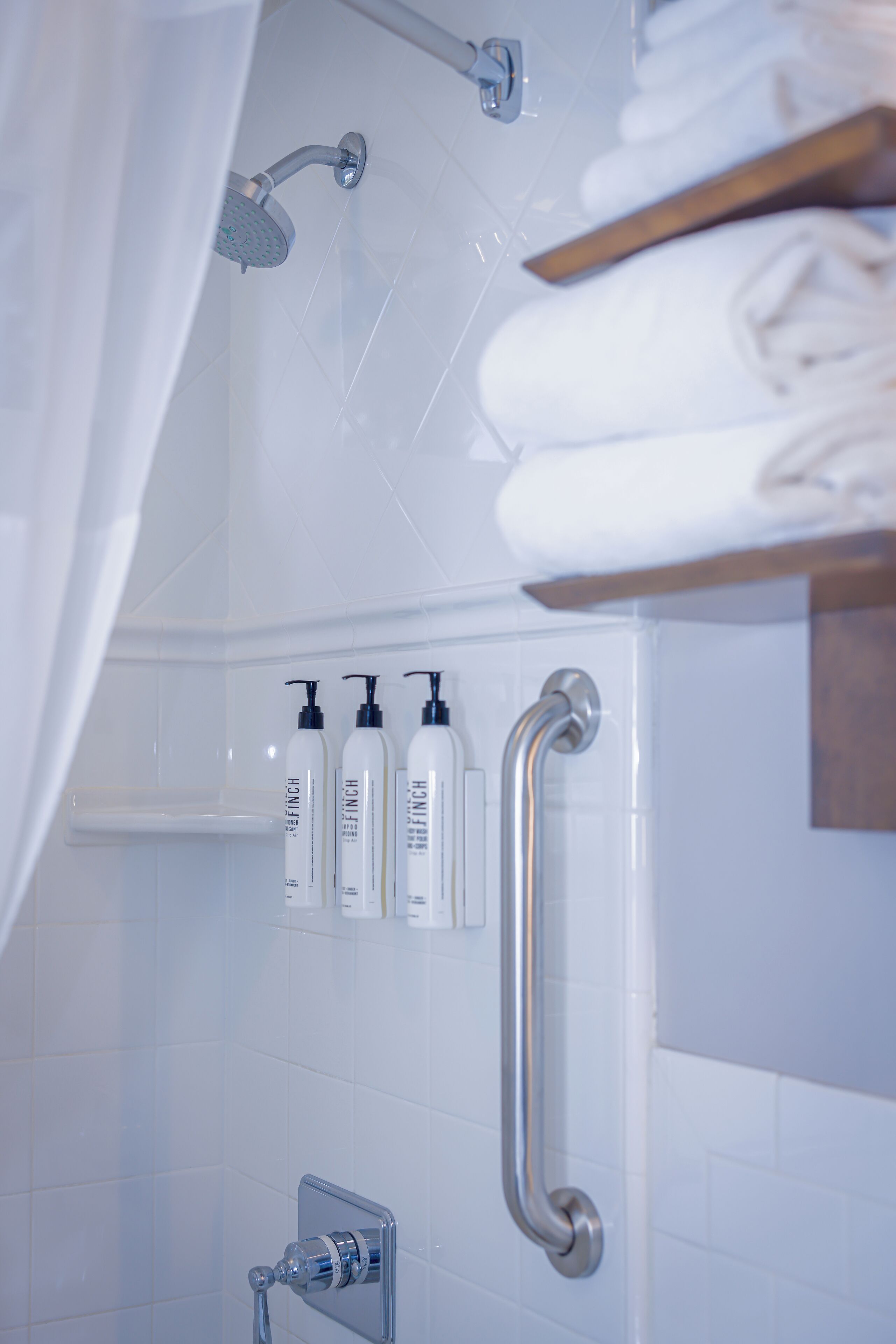 A modern bathroom with a shower, grab bars, and neatly arranged toiletries on a shelf.