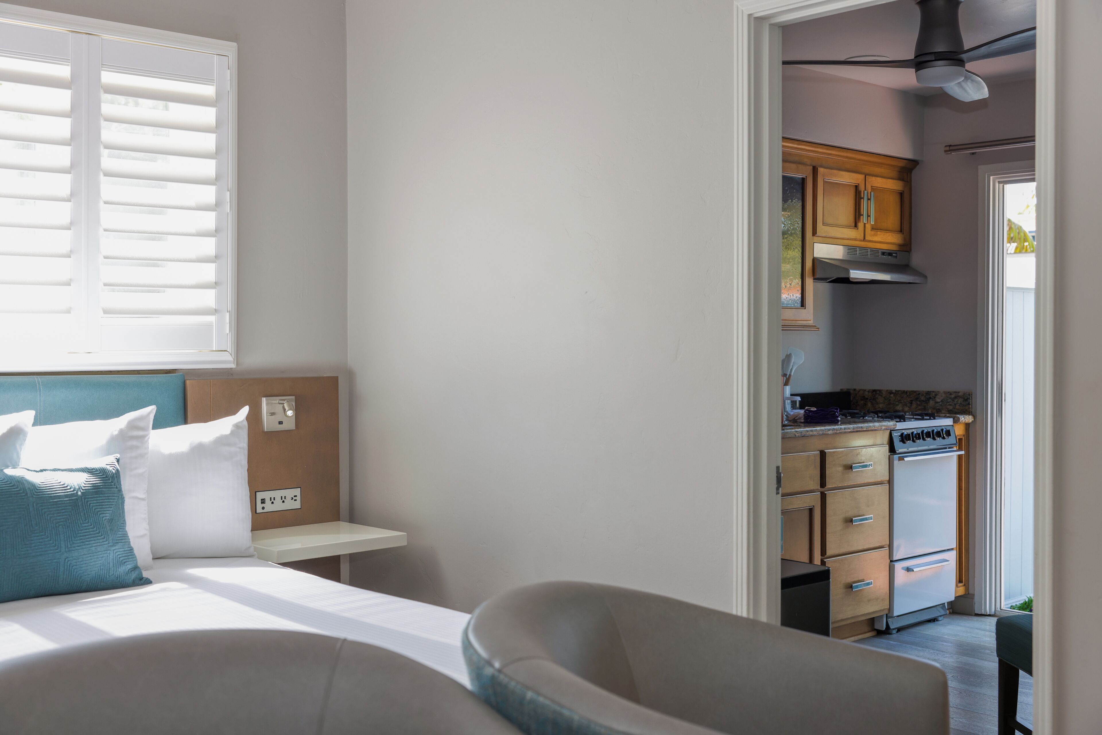 A bedroom with a bed, bedside table, and a view into a kitchen area.