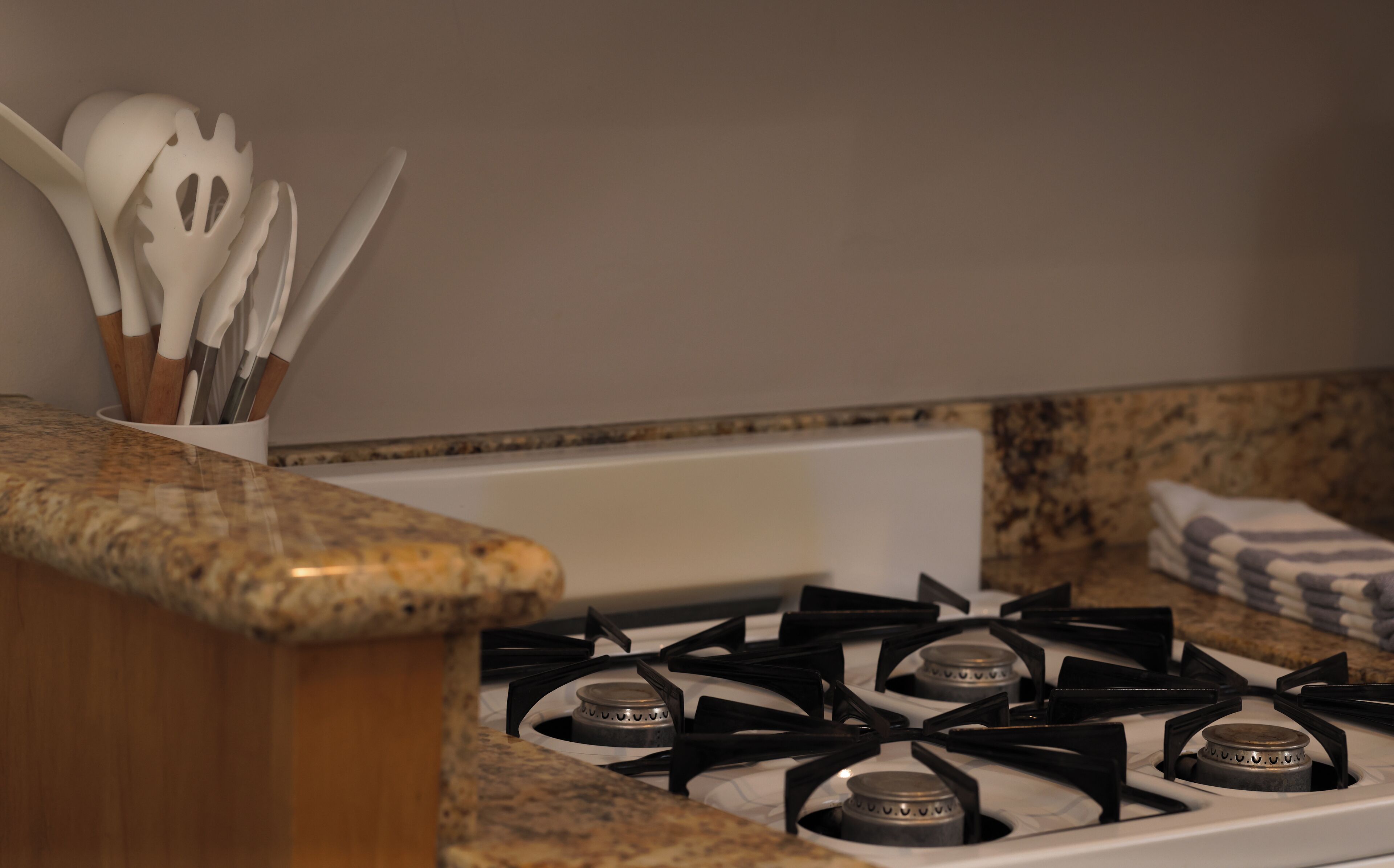 A kitchen with a gas stove, a white sink, and a granite countertop.