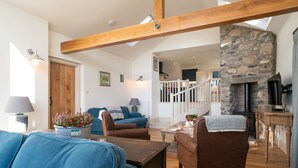 Amplia sala de estar con techo alto, vigas de madera, chimenea de piedra y vista al piso superior.