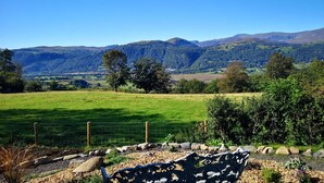 Un paisaje rural con un campo cercado, una manta estampada y montañas a lo lejos.