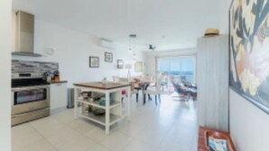 A modern kitchen with a built-in oven, a dining area with a table and chairs, and a large window providing a view. - Unobstructed Ocean View - Ocean Front Condo (Sint Maarten)