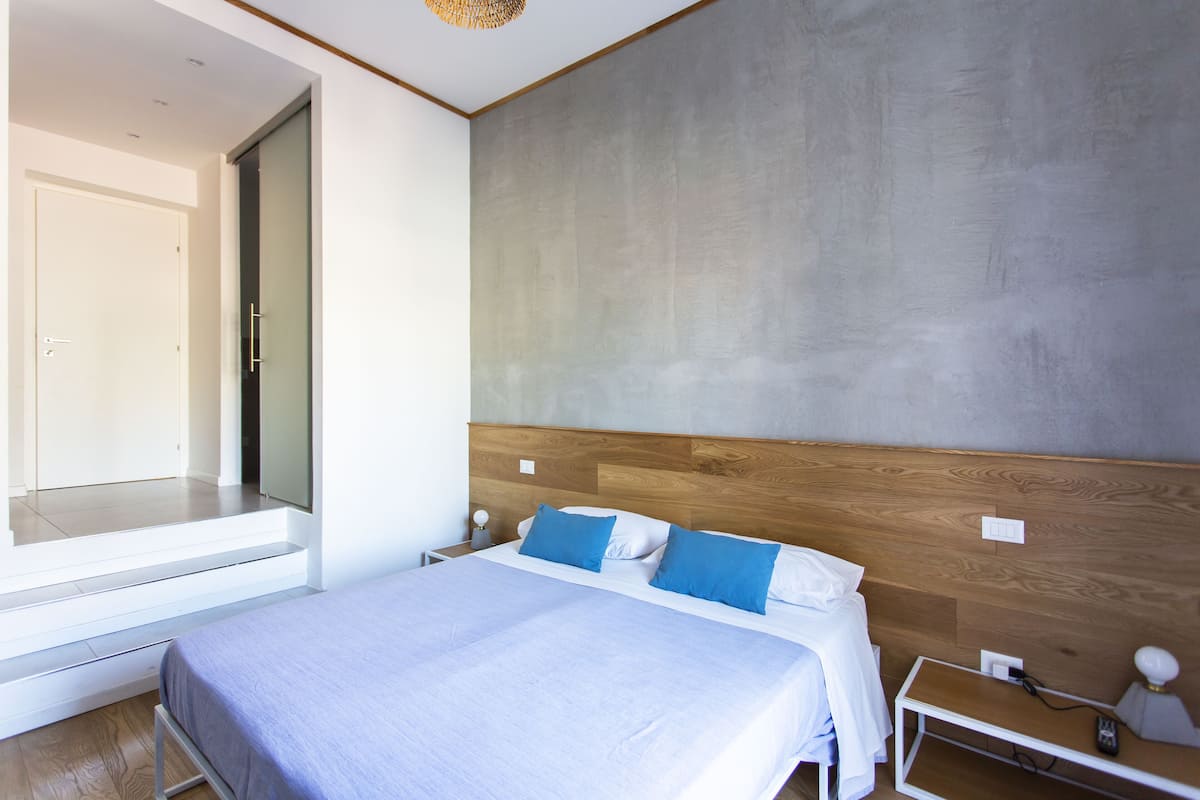 A modern bedroom with a large bed, a wooden headboard, and a view of a balcony.