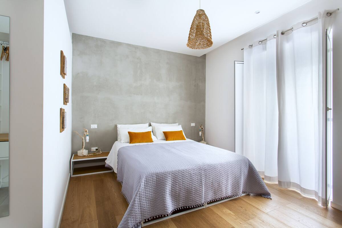 A modern bedroom with a large bed, wooden flooring, and a hanging light fixture.